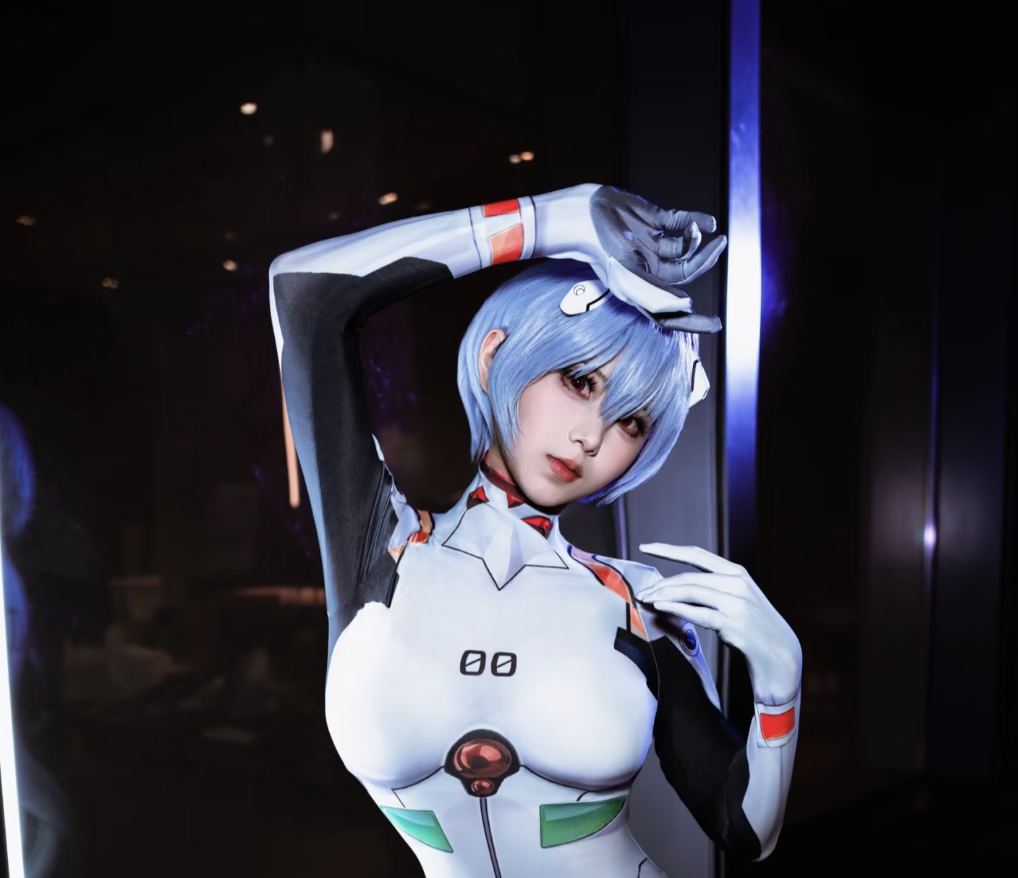 A person showcasing a hot cosplay as Rei Ayanami from Neon Genesis Evangelion, wearing a white and black plug suit with a blue wig, poses with one hand on their head and the other near their face against a dark background.