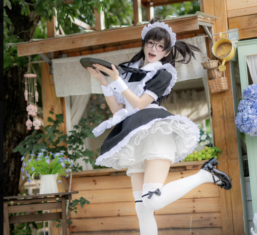 A person in a sexy maid black and white outfit and glasses poses cheerfully outdoors, holding a serving tray, with greenery and wooden structures in the background.
